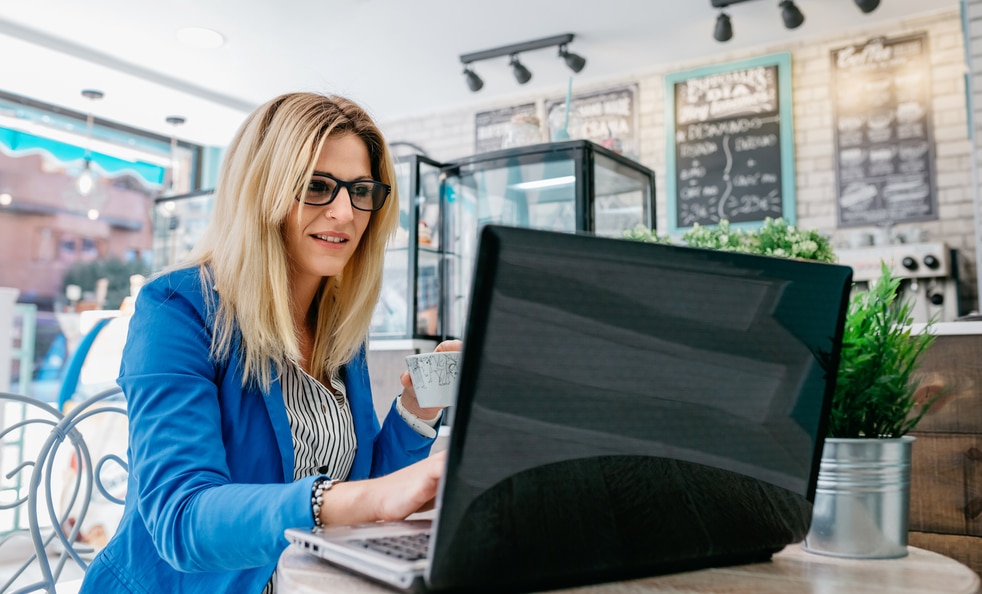 Woman drinking coffee and chatting with the laptop in a coffee shop